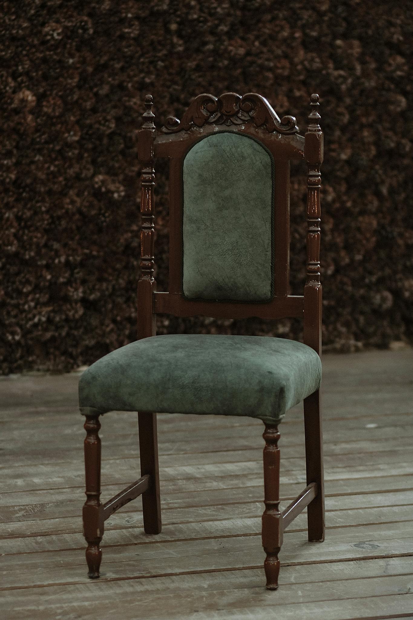 A green upholstered wooden chair with intricate carvings on an outdoor wooden deck.